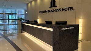 A reception desk at the Centum Business Hotel with a modern design, a logo above the desk, and a glass entrance in the background. - Centum Business Hotel (Busan)