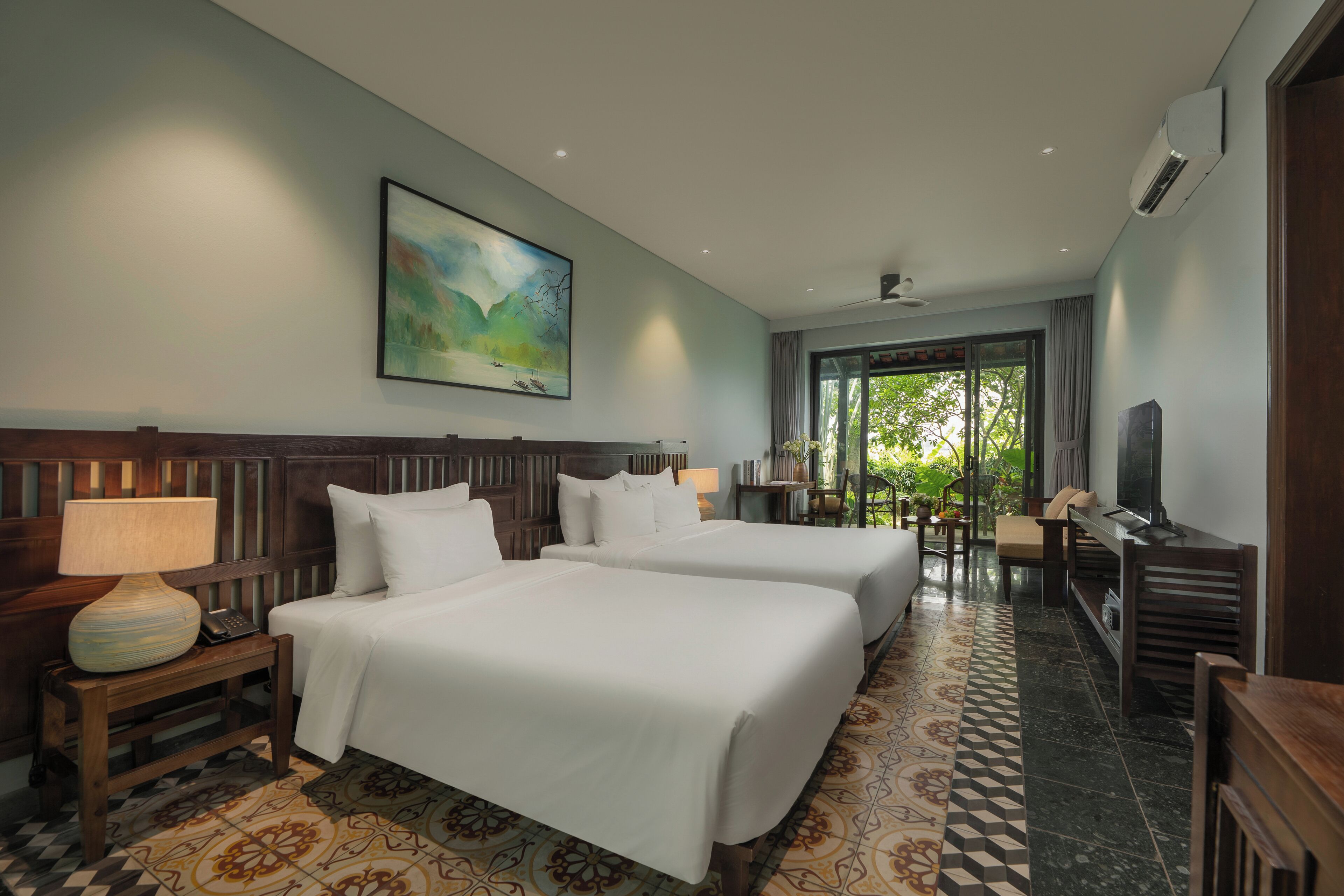 A hotel room with two beds, a desk, a chair, a TV, and a painting on the wall.