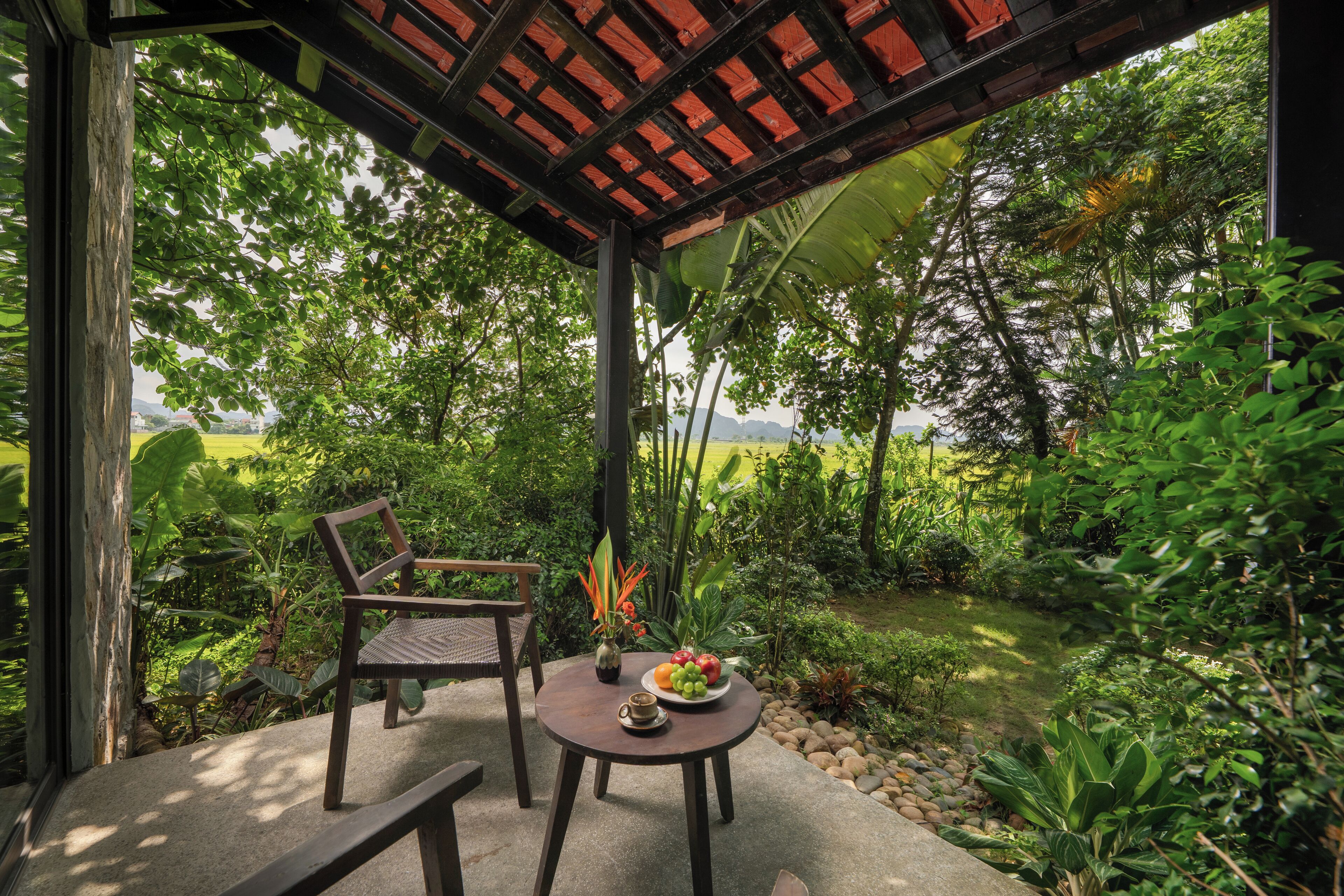 A covered patio with a table and chairs, surrounded by lush greenery and a view of a distant landscape.