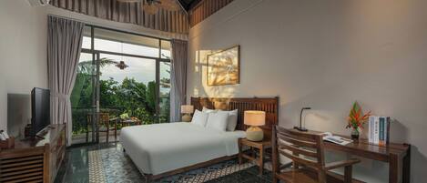 Habitación de hotel con una cama grande, un escritorio con lámpara, un televisor y vistas a zonas verdes.