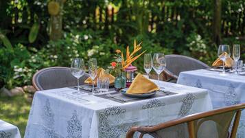 A table set outdoors with lace tablecloths, wine glasses, and a vase with flowers.