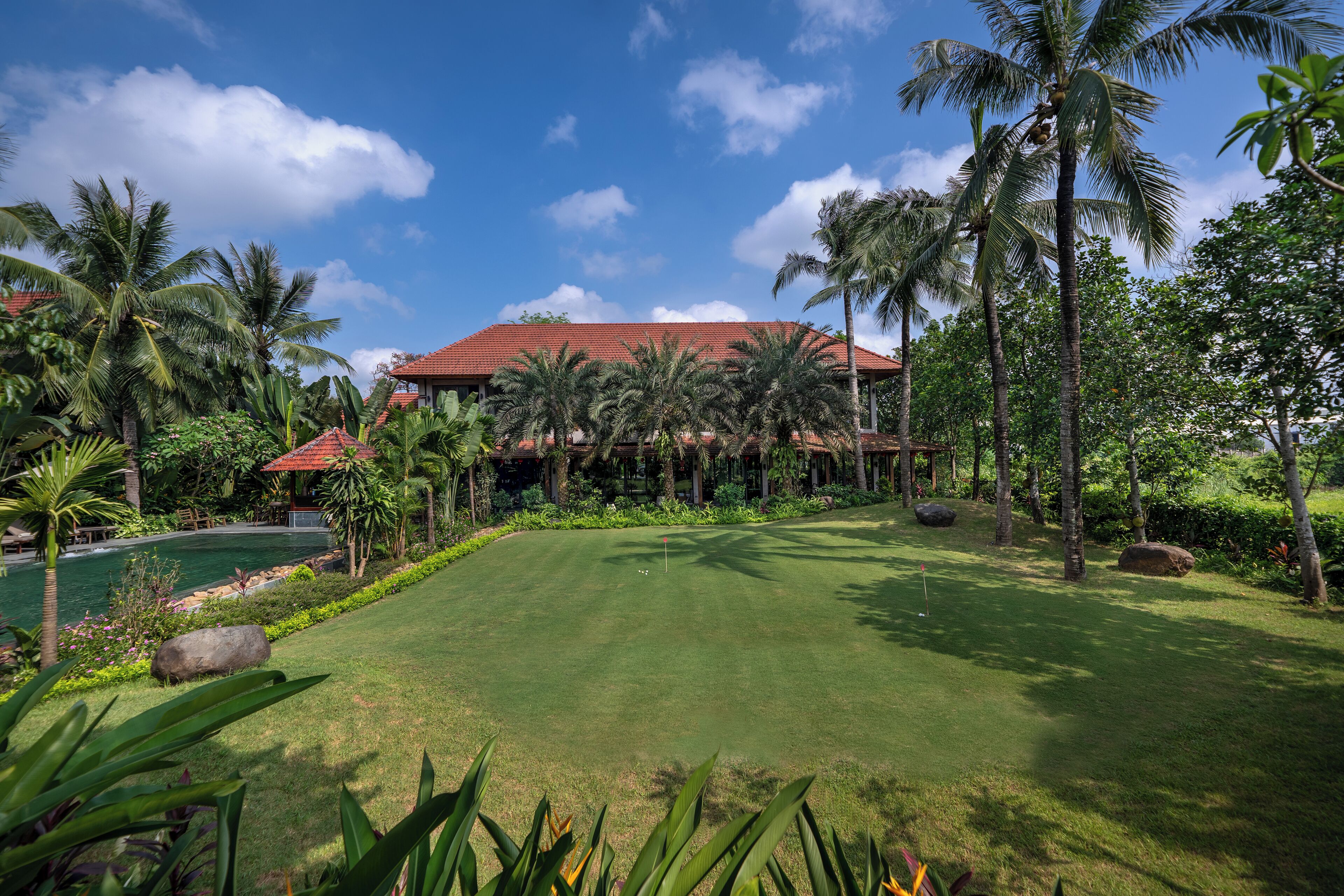 Un campo de golf bien cuidado con vista despejada al club de campo, rodeado de exuberante vegetación y palmeras.