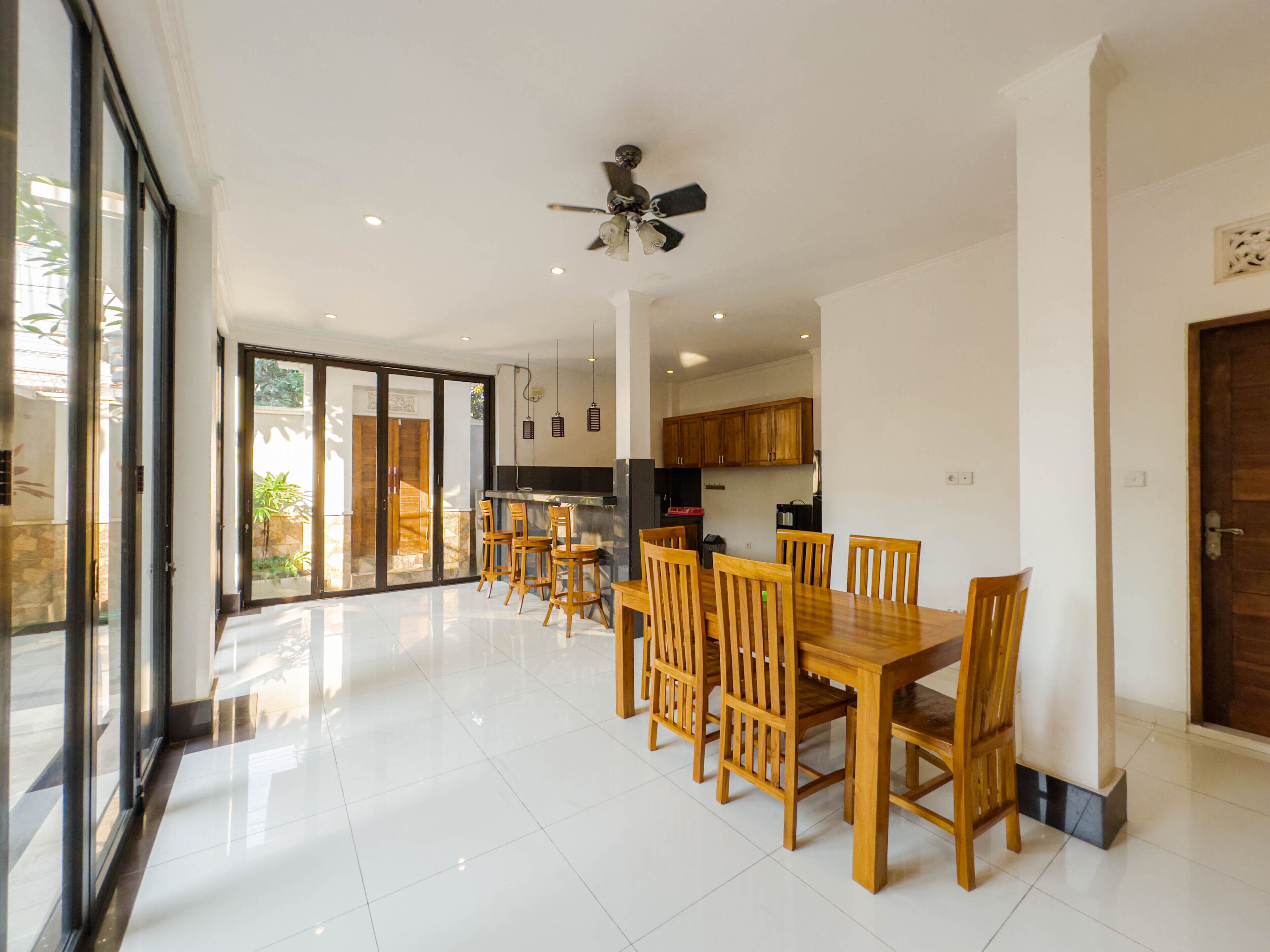 A spacious dining area with a large wooden table and chairs, a ceiling fan, and a kitchen in the background.