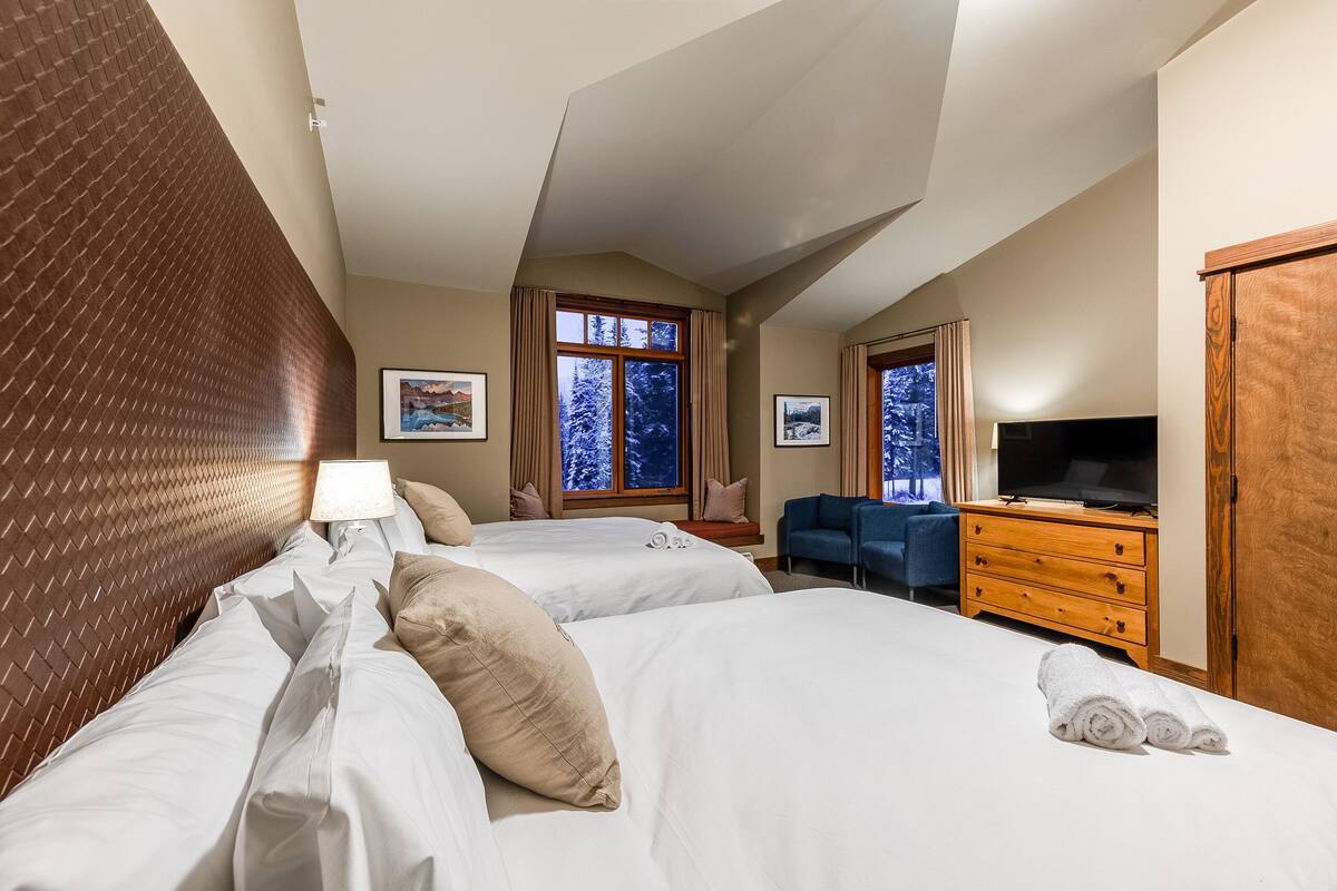 Quarto de hotel com duas camas, televisão, penteadeira e janela com vista para a neve.