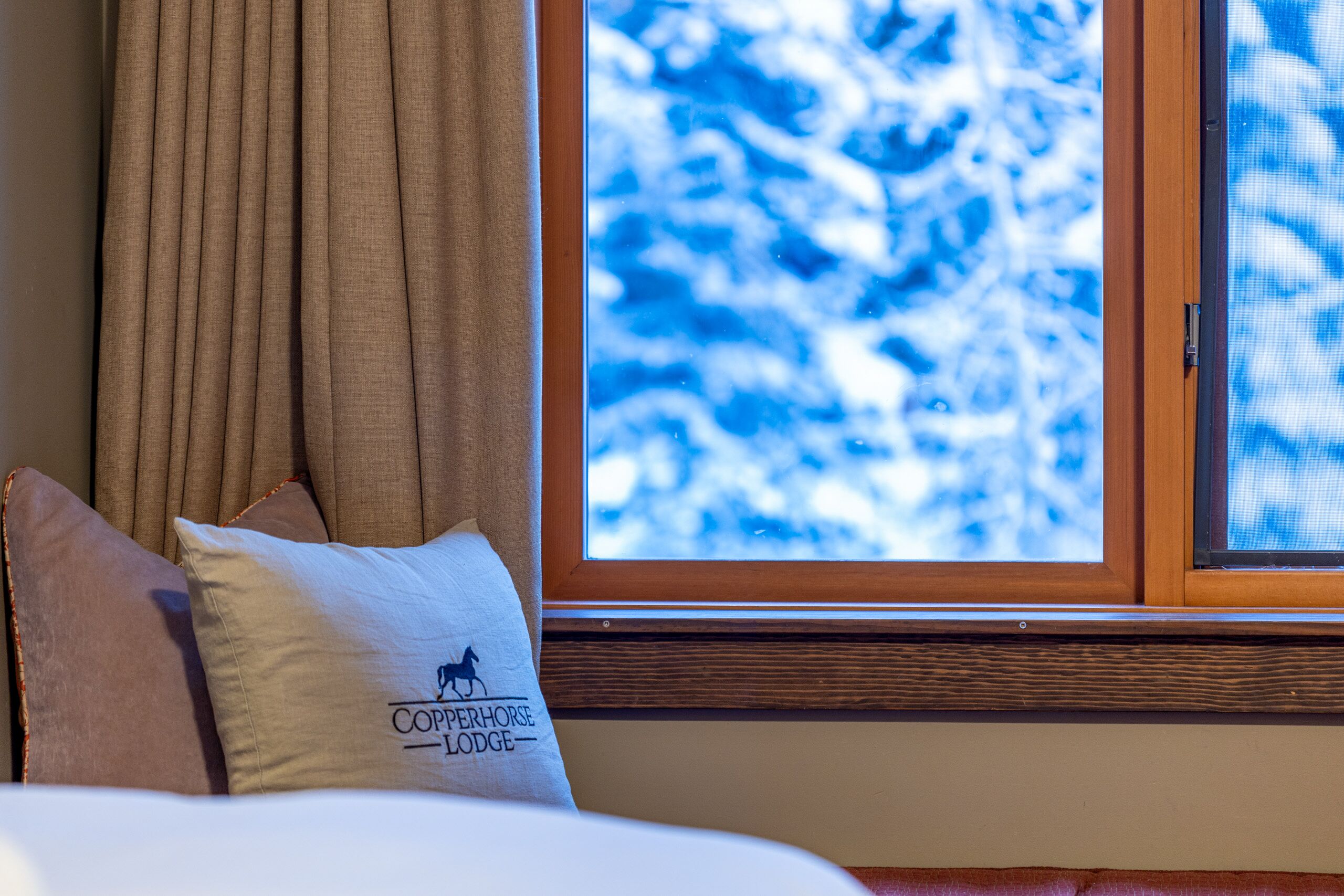 Une chambre d’hôtel avec une fenêtre donnant sur des arbres couverts de neige, un lit avec deux oreillers et une tête de lit en bois.