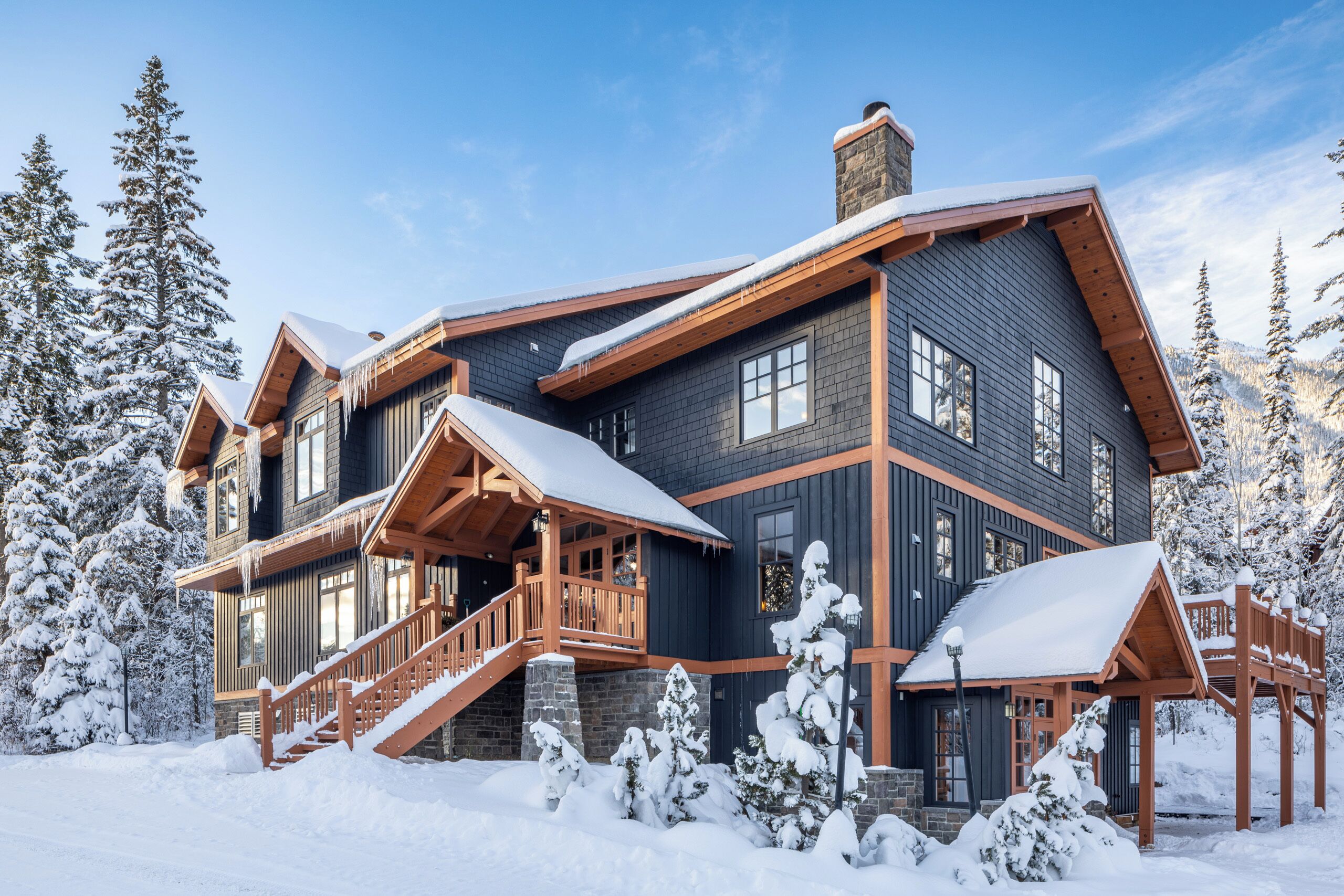 Un gran alojamiento de varios pisos con una llamativa escalera de madera y un balcón, rodeado de árboles cubiertos de nieve.
