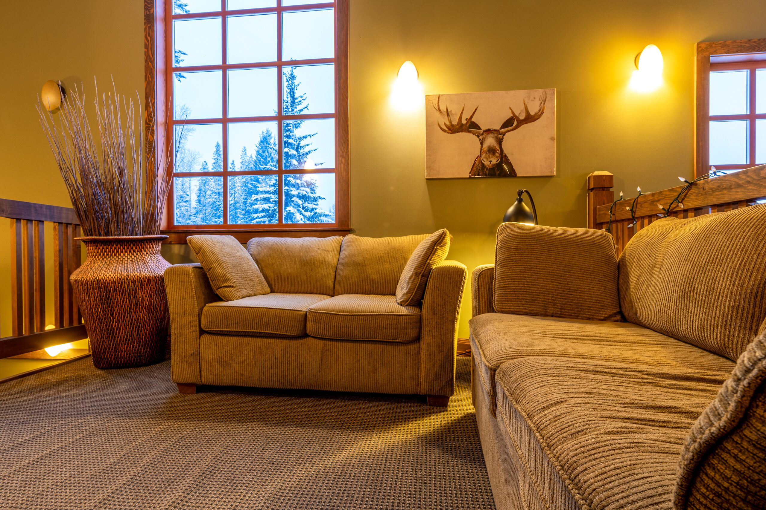 A cozy living room with a large window, a sofa, a lamp, and a decorative wall piece.