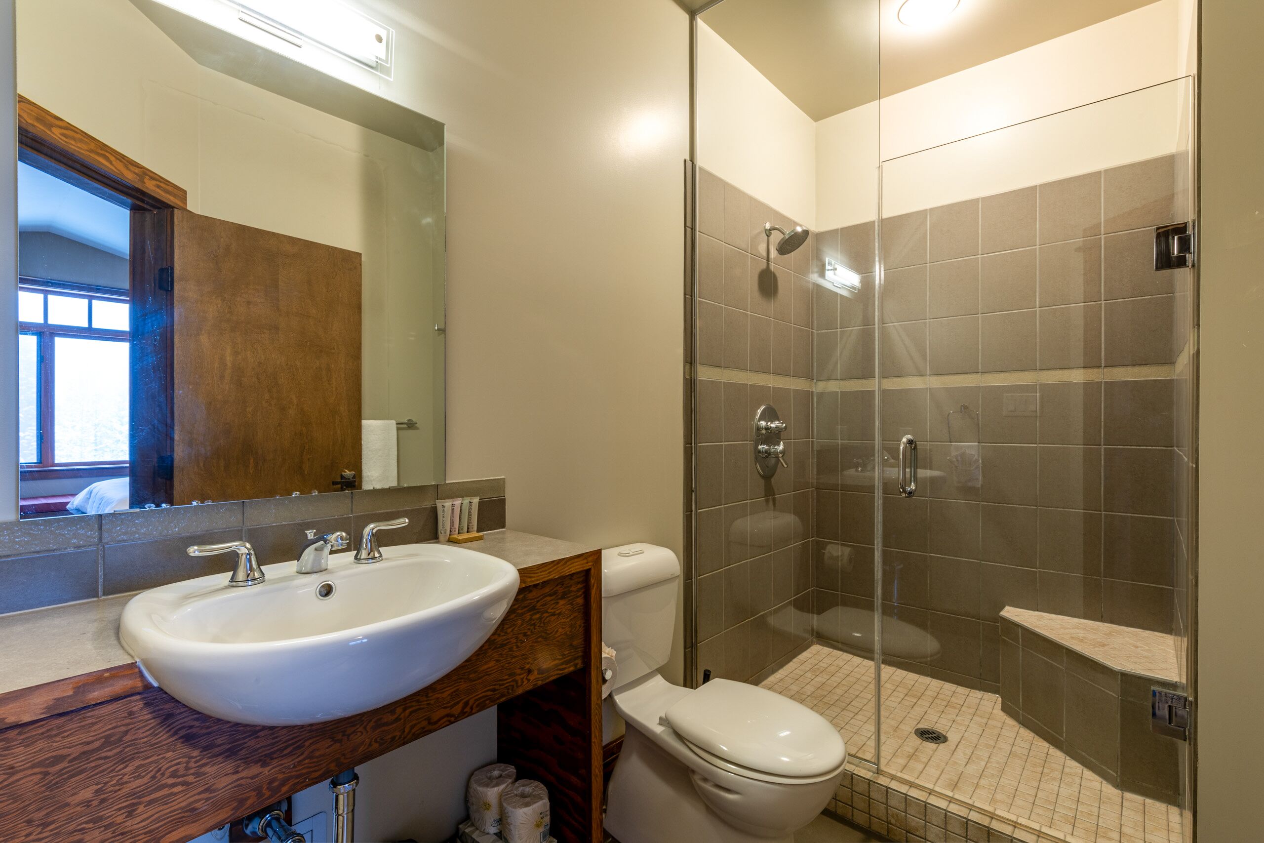 A modern bathroom with a white sink, wooden vanity, a toilet, and a glass-enclosed shower area.
