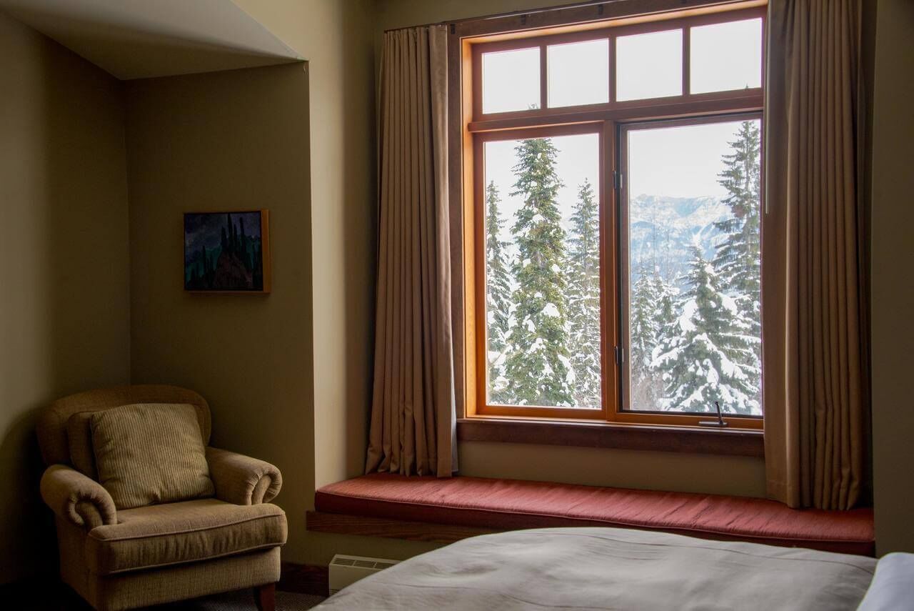A room with a large window, a chair, a bed, and a painting on the wall.