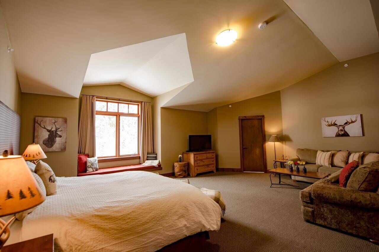 Een ruime slaapkamer met een groot bed, een sofa, een televisie en een raam met gordijnen.