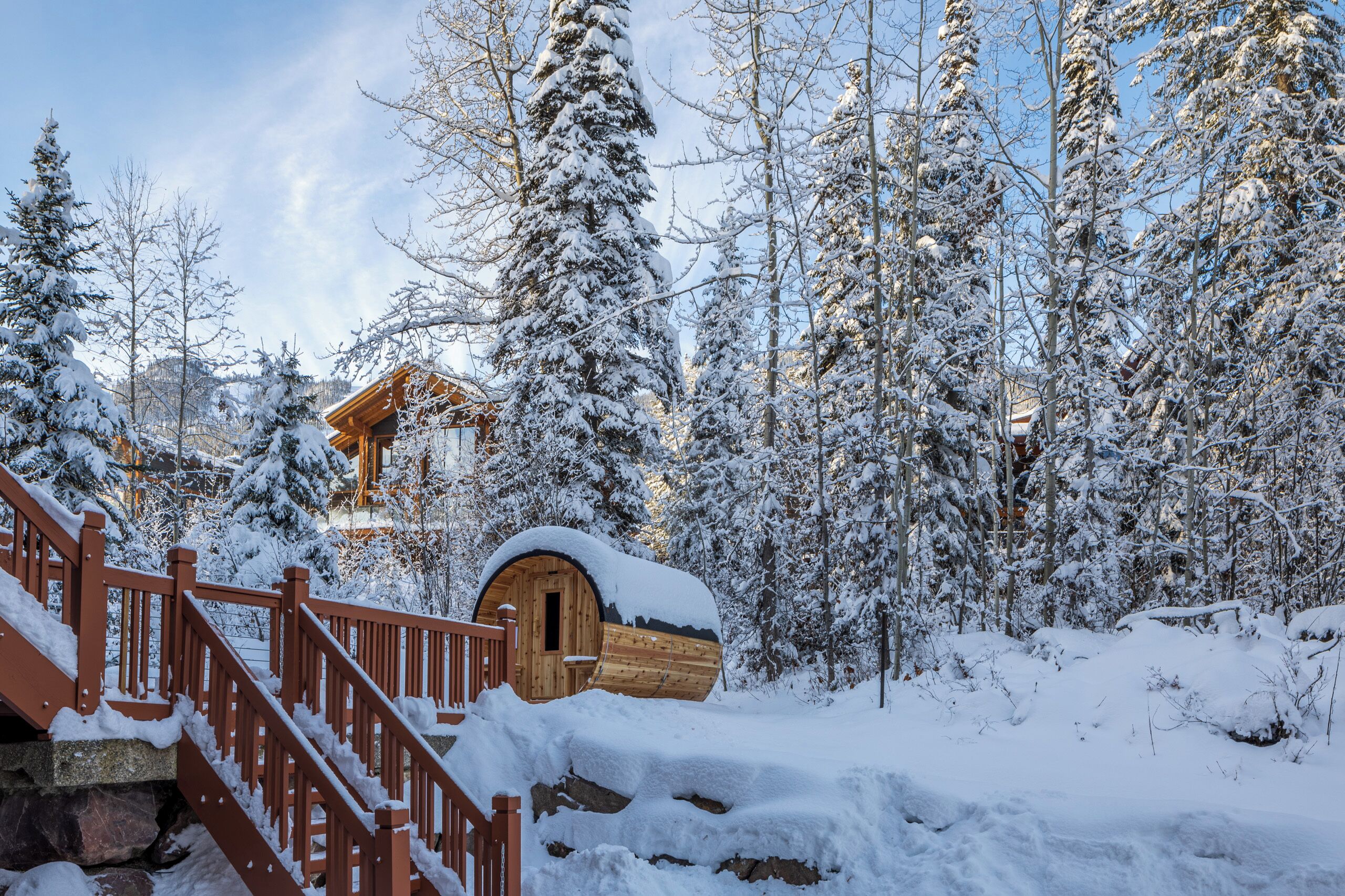 Una cabaña de madera con techo cubierto de nieve, rodeada de árboles cargados de nieve y una escalera de madera que lleva a ella.