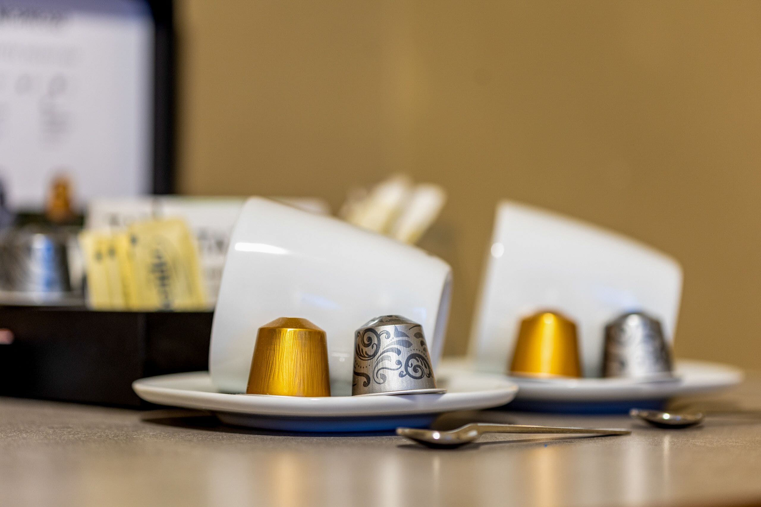 A table setting with a white plate, a gold-colored condiment container, and a silver patterned condiment container.