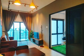 A modern living room with a sofa, a coffee table, and a TV. There is a balcony with a view of the city. - Reizz Residence by Plush (Kuala Lumpur)