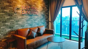 A modern living room with a brick wall, a leather sofa, a small table, and a large window offering a city view. - Reizz Residence by Plush (Kuala Lumpur)