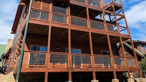 Una cabaña de madera de varios niveles con balcones y ventanas amplias, ubicada en una ladera.