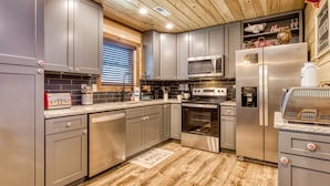 Una cocina moderna con electrodomésticos de acero inoxidable, gabinetes grises y techo de madera.
