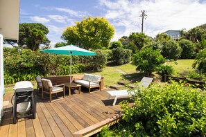 Um deck de madeira com móveis externos, uma cadeira de rodas e um guarda-sol verde.