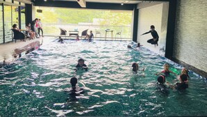 Una piscina interior con agua cristalina, rodeada de zonas de estar y vistas a zonas verdes exteriores.