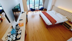 Habitación de hotel con cama, escritorio con televisor, silla y mesa con vistas al exterior.