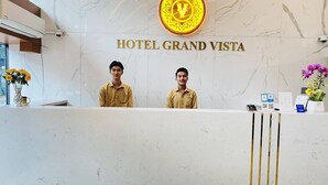 Mostrador de recepción en el Hotel Grand Vista con dos empleados, una pared de mármol y un logotipo sobre el área de recepción.
