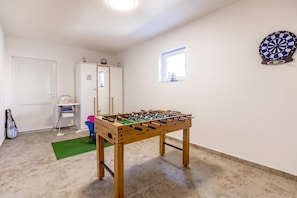 Una habitación con mesa de futbolín, dardo y una ventana y puerta.