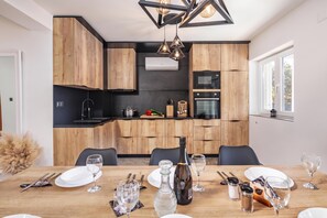 A modern kitchen with wooden cabinets, a built-in oven, and a dining area set for a meal. - Pool House Beba Tribalj Lake, Tribalj, Croatia (Tribalj)