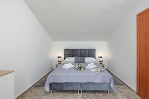 Une chambre à coucher avec un lit, des tables de chevet, une commode, une porte en bois et une petite étagère.