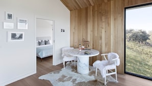 Una habitación moderna con techo de madera, una mesa redonda de mármol, sillas blancas y un ventanal con vistas a un campo cubierto de césped.