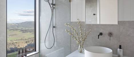 A bathroom with a large window, a shower, a sink, and a mirror.