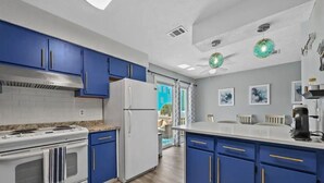 A kitchen with blue cabinets, white appliances, and a view to the outside. - CUTE! little end-unit beach townhome (Panama City Beach)