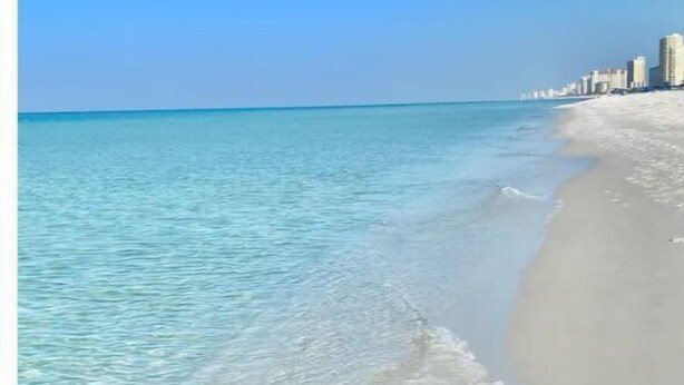 A beach with clear blue water and a city skyline in the background. - CUTE! little end-unit beach townhome (Panama City Beach)