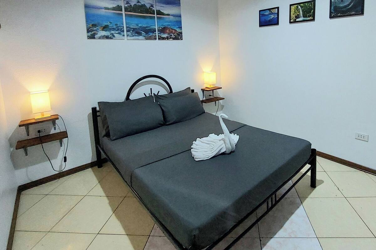 A bedroom with a bed, two bedside lamps, and three framed pictures on the wall.