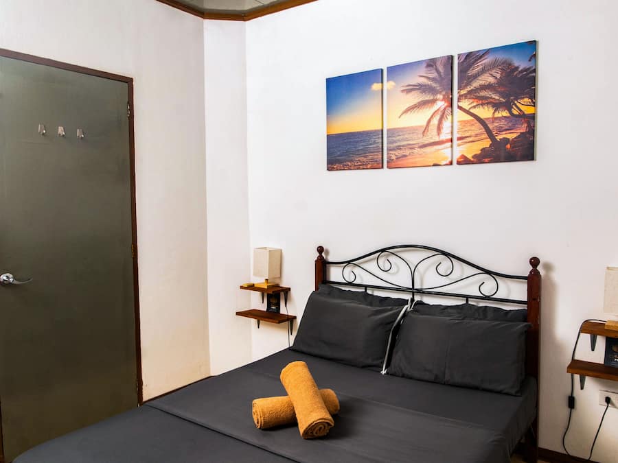 A bedroom with a bed, a door, a nightstand with a lamp, and a wall with a sunset painting.