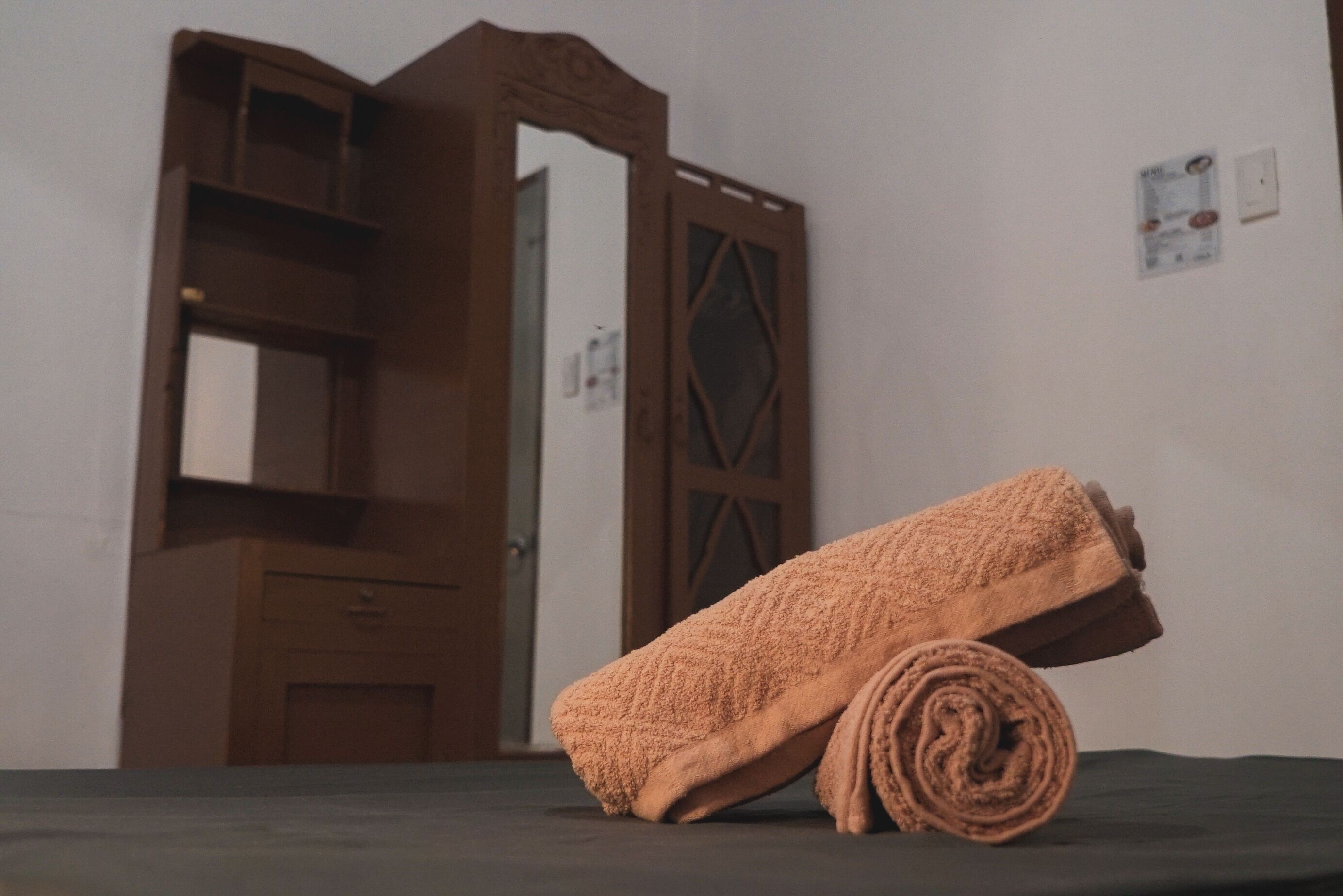 A room with a wooden door, a mirror, and a rolled-up towel on a dark surface.