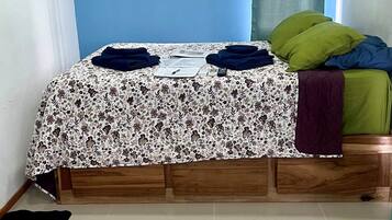 Un dormitorio con cama, pared azul con el texto 'PURA VIDA', ventana con cortinas y un equipo de aire acondicionado.