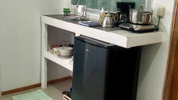 Cocina compacta con refrigerador, pileta y ventana con cortina verde.