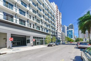 A multi-story hotel with a modern design, featuring balconies on each floor and a parking area in front.