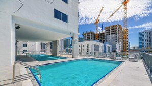 A rooftop pool with clear blue water, surrounded by modern buildings and construction cranes. - Designer 1BR | 24th Floor Gym | Brickell Core (Miami)