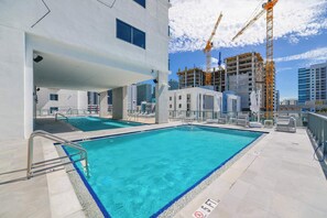 A rooftop pool with clear blue water, surrounded by modern buildings and construction cranes. - Designer 1BR | 24th Floor Gym | Brickell Core (Miami)
