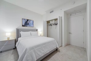 A bedroom with a bed, nightstands, a wardrobe, and a painting on the wall. - Designer 1BR | 24th Floor Gym | Brickell Core (Miami)