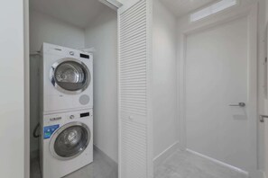 A compact laundry room with a front-loading washer and dryer, a white door, and a tiled floor.
