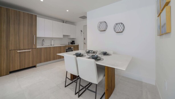 A modern kitchen with white cabinets, a wooden countertop, and a dining area with a white table and chairs. - Designer 1BR | 24th Floor Gym | Brickell Core (Miami)