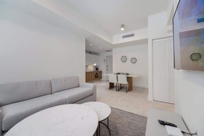 A modern living room with a grey sofa, a dining table with chairs, a kitchen area, and a white wardrobe. - Designer 1BR | 24th Floor Gym | Brickell Core (Miami)