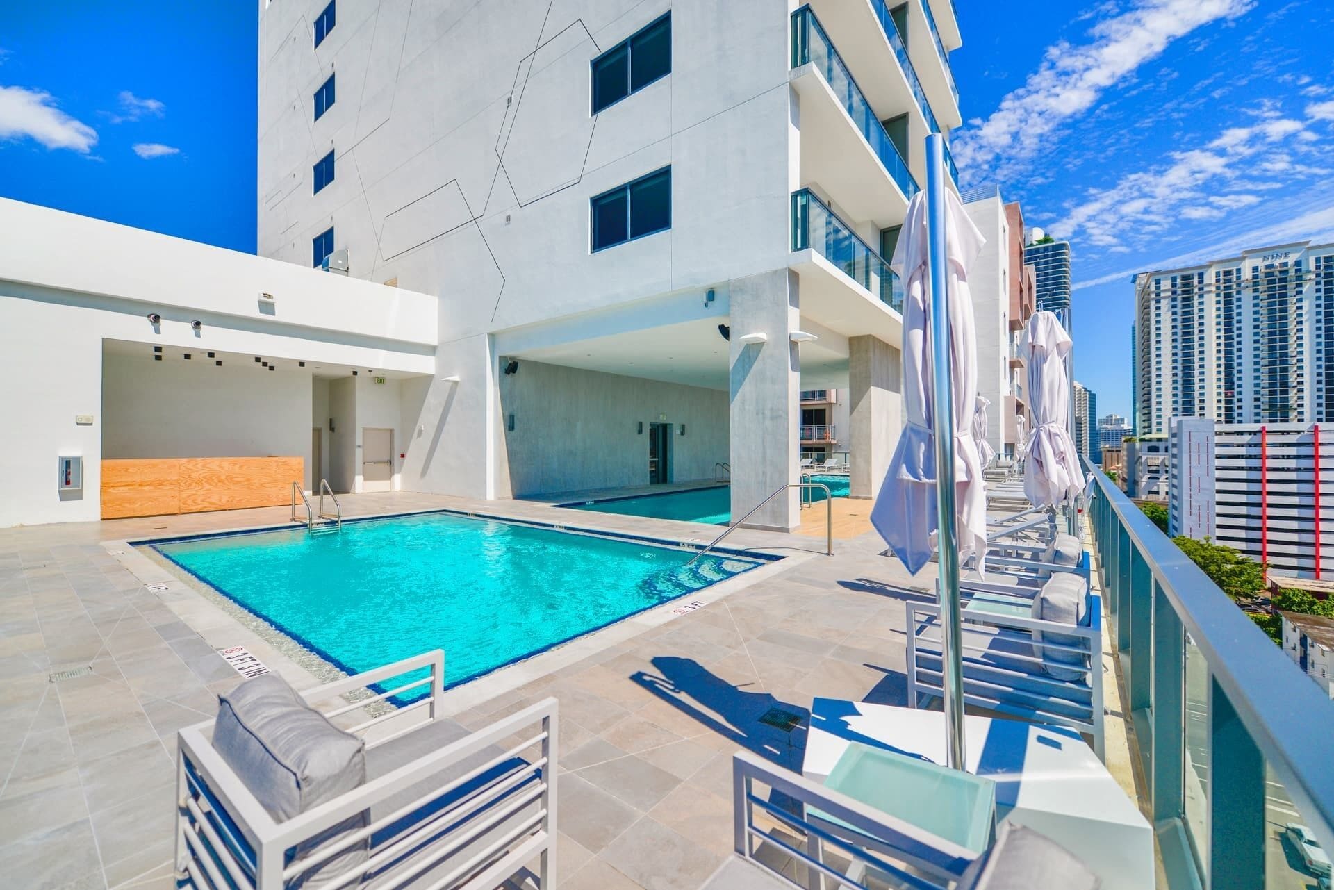 A rooftop pool area with a clear blue pool, sun loungers, and a view of the city skyline.