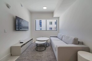 A modern, minimalist living room with a grey sofa, a small round table, and a TV mounted on the wall.