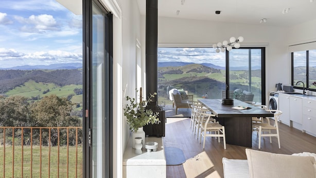 A modern kitchen with a large island, a dining area with chairs, and a view of the countryside. - The Bella Vista by Mt Bellevue - with spa and spectacular views. (Myrrhee)
