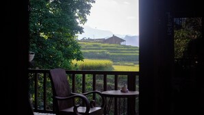 A balcony with a wooden chair and table, overlooking a green field and distant mountains. - Ta Van (Ta Van)