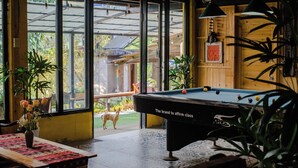 A pool table with a brand name, a dog outside the window, and indoor plants. - Ta Van (Ta Van)
