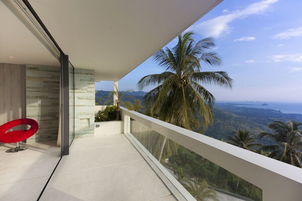 Un balcon doté d’une balustrade en verre, offrant une vue sur un paysage montagneux et des palmiers.