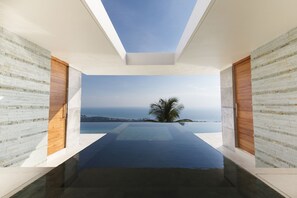 Un intérieur moderne agrémenté d’une verrière, d’une piscine et offrant une vue sur la mer.